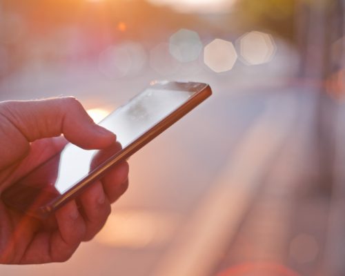 Man using mobile smartphone. Close up of a businessman hand holding and using a smart phone outdoors. Detail of handsome hipster modern businessman using smart phone in the city