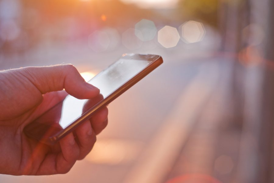 Man using mobile smartphone. Close up of a businessman hand holding and using a smart phone outdoors. Detail of handsome hipster modern businessman using smart phone in the city